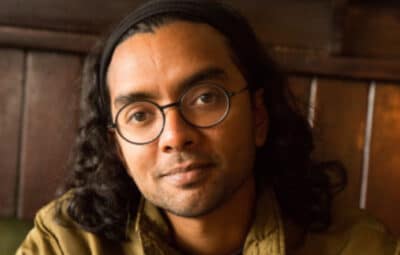 Poet Arji, close up of a mans face with round black rimmed glasses, long dark hair