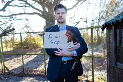 a man holding a chicken and a sign that says 'I am god'