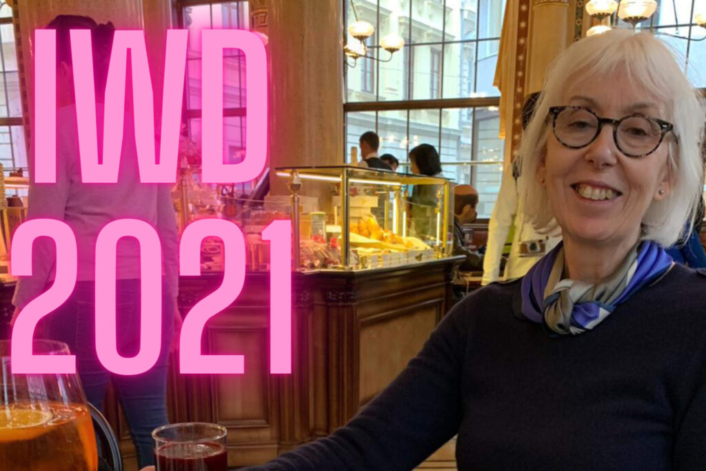Woman sat in a bar with larger pink letters saying IWD 2021