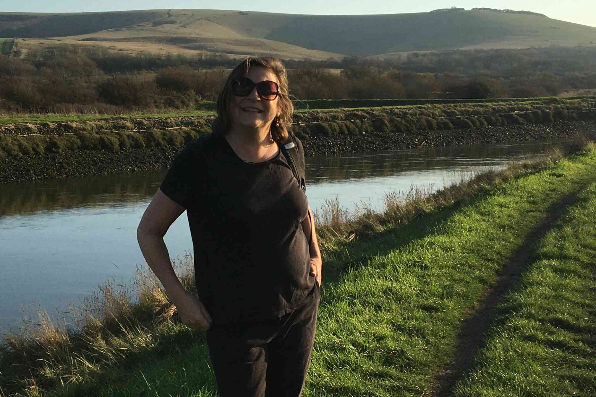 Woman in sunglasses in front of the river as sun goes down