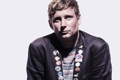 Man looking at camera, short hair and jacket covered in badges.