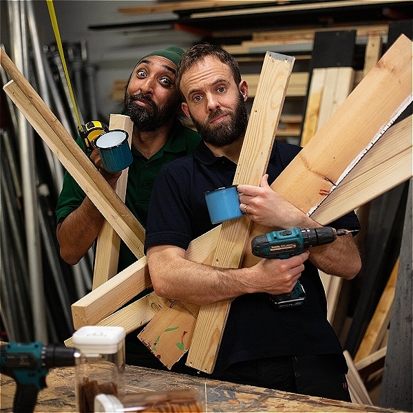Two men hold lots of planks of wood and tools
