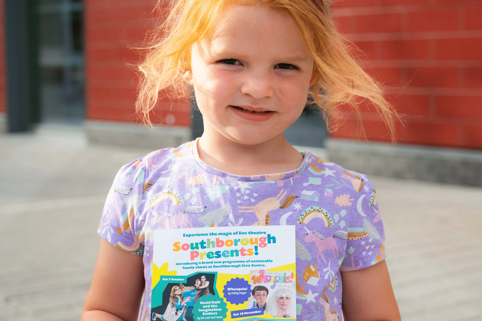 A young girl with red hair is holding a Southborough Presents flyer.