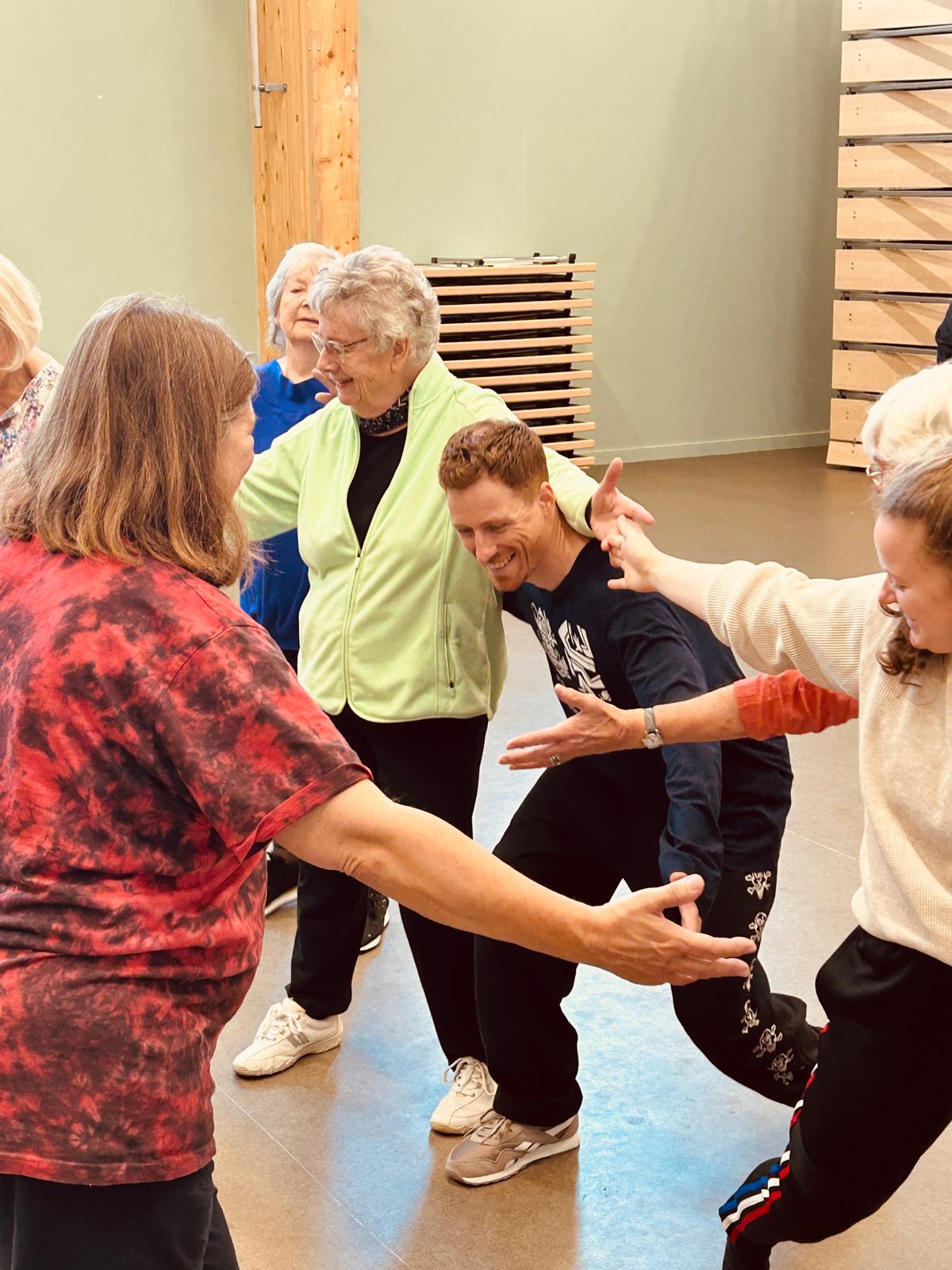 A group of people dancing together. Their arms are outstretched towards each other and they are smiling