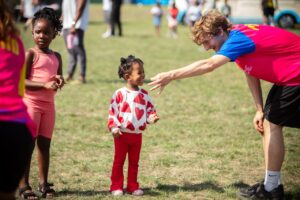 A performer wearing a colourful t shirt reaches out to a young girl who is smiling