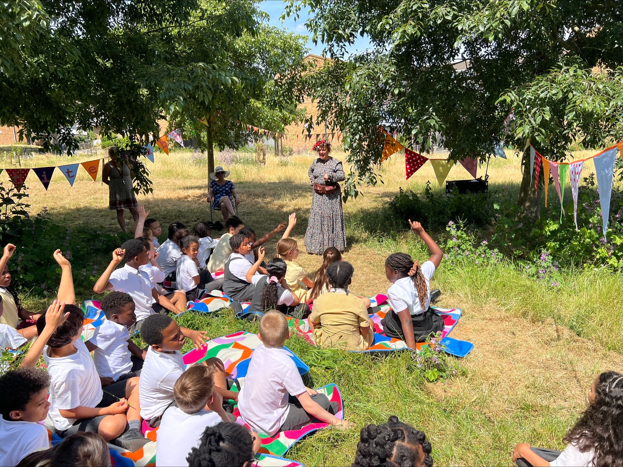 Performer Bernadette Russell stands in front of children seated in front of her in a field