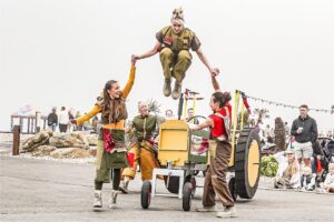 Three performers dance around a large model tractor as part of an outdoor touring dance theatre performance
