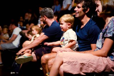 Audience watching a show. A child is sat on an adult's lap smiling