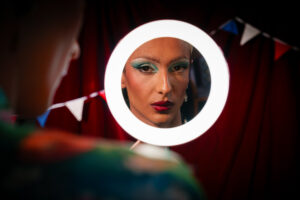 Close up of performer looking into the reflection of a mirror with a ring light around it